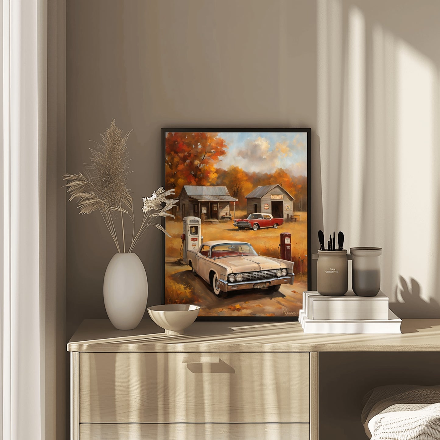 Framed vintage gas station artwork featuring classic cars and autumn scenery displayed on a wooden dresser